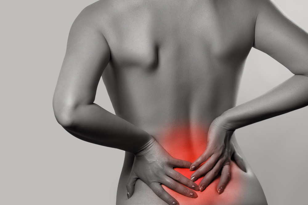 Woman having backache, pain back isolated on gray background. Scoliosis. Spinal cord problems on womans back. Beautiful naked woman touching her back. Chiropractor North Lakes